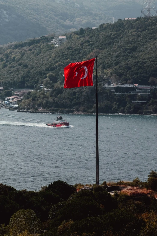 a large boat travels down a river past a flag