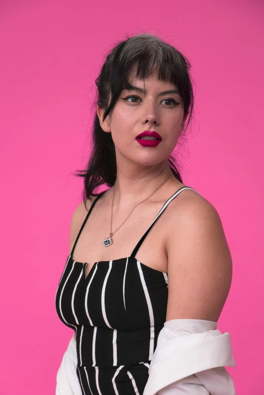 a woman wearing striped dress standing up against a pink background