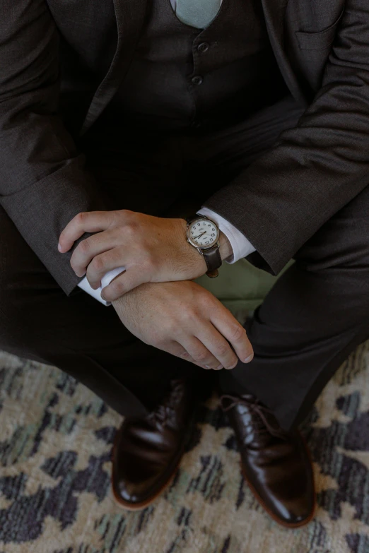 a man in a suit is sitting down and tying his watch