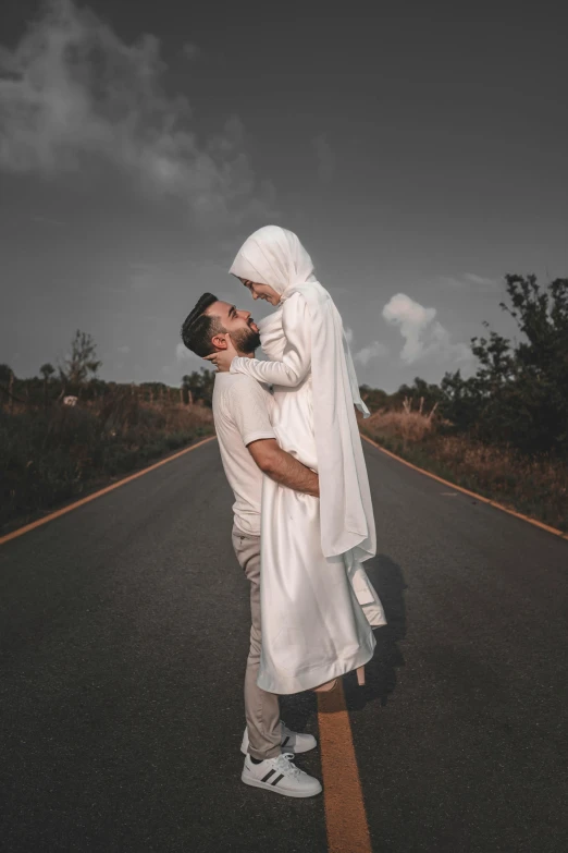 a young woman wearing a white dress and a veil emces her man on the road