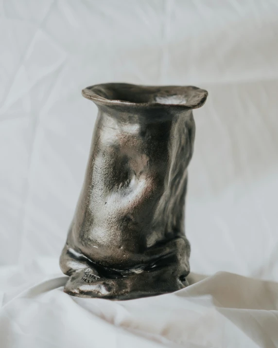 a grey vase sitting on a white sheet