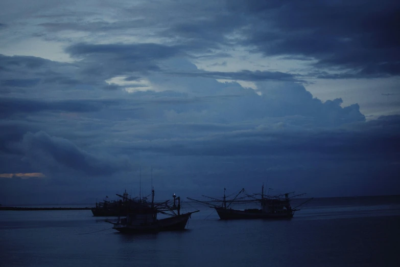 two boats anchored in the water under an overcast sky