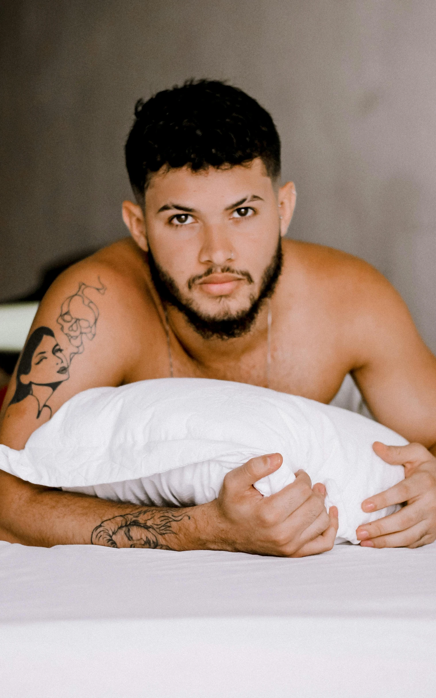 shirtless man laying on bed with white sheets and a pillow