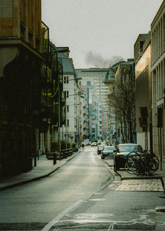 a long narrow street has parked cars and bicycle racks