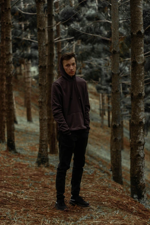 a young man in a hoodie poses for the camera, surrounded by trees