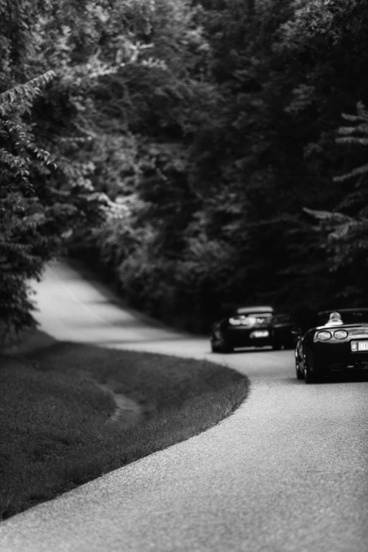 black and white image of three cars on a road