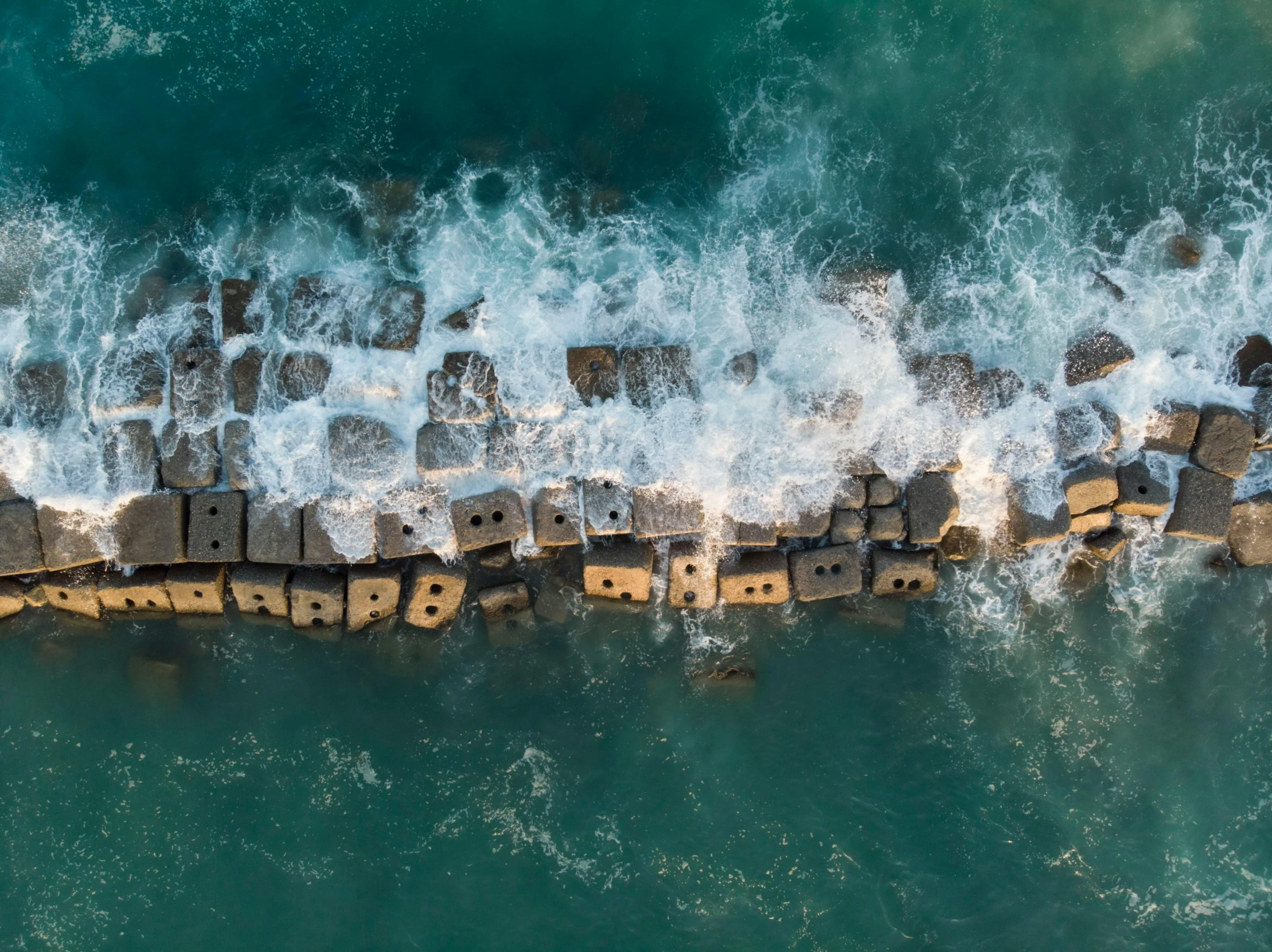 a seawall next to a beach with waves hitting it