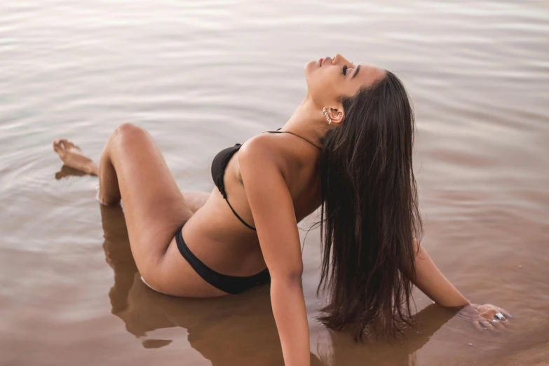 a girl laying down in a lake in a black bikini