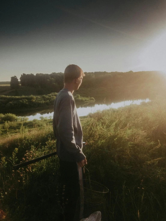 the boy looks over the meadow at the river