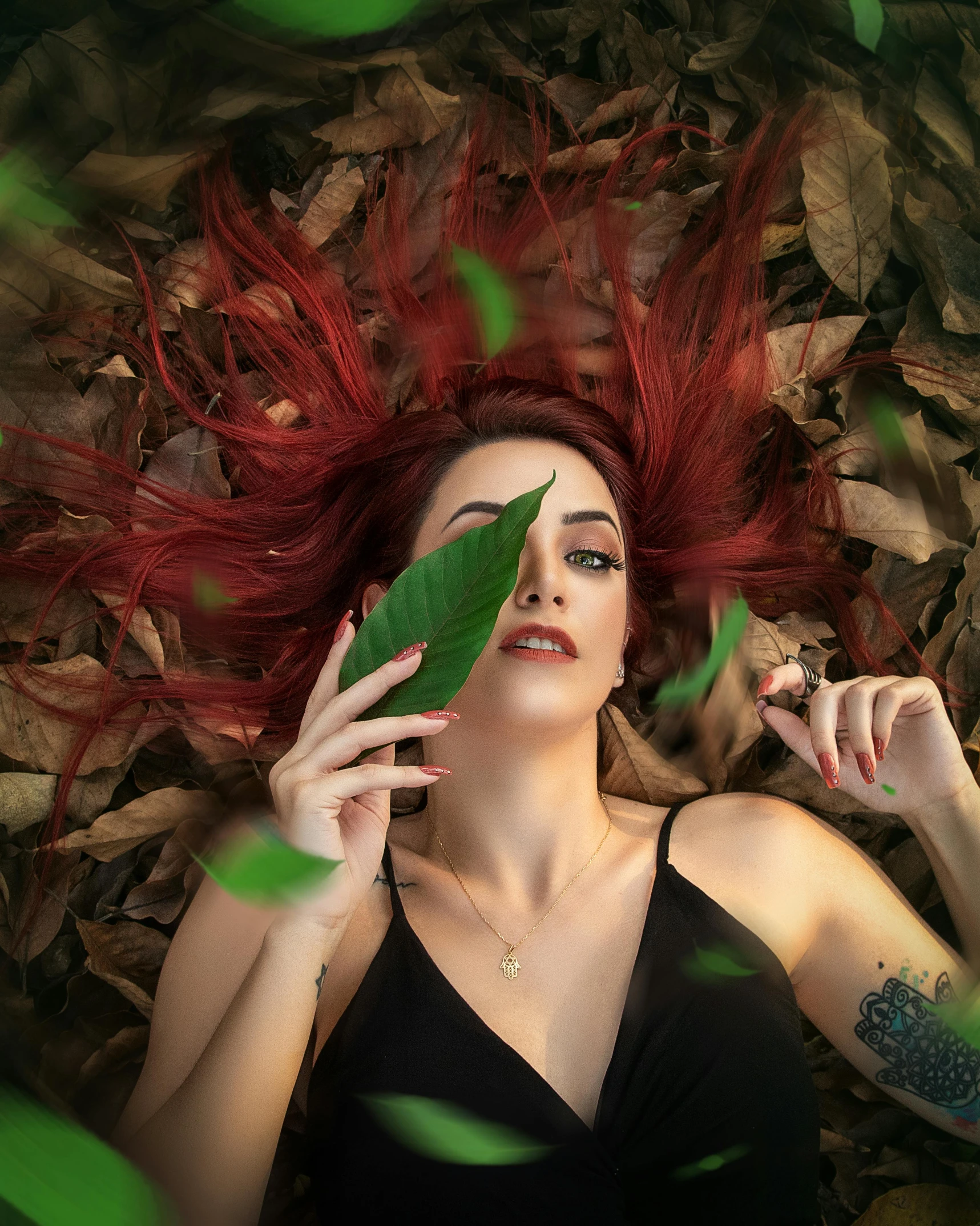 woman with red hair and tattoos holds up a leaf to her face