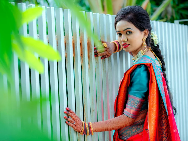 a woman is standing by a white fence and holding a flower