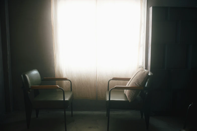 two chairs are in a dimly lit room with the sun beaming through the window