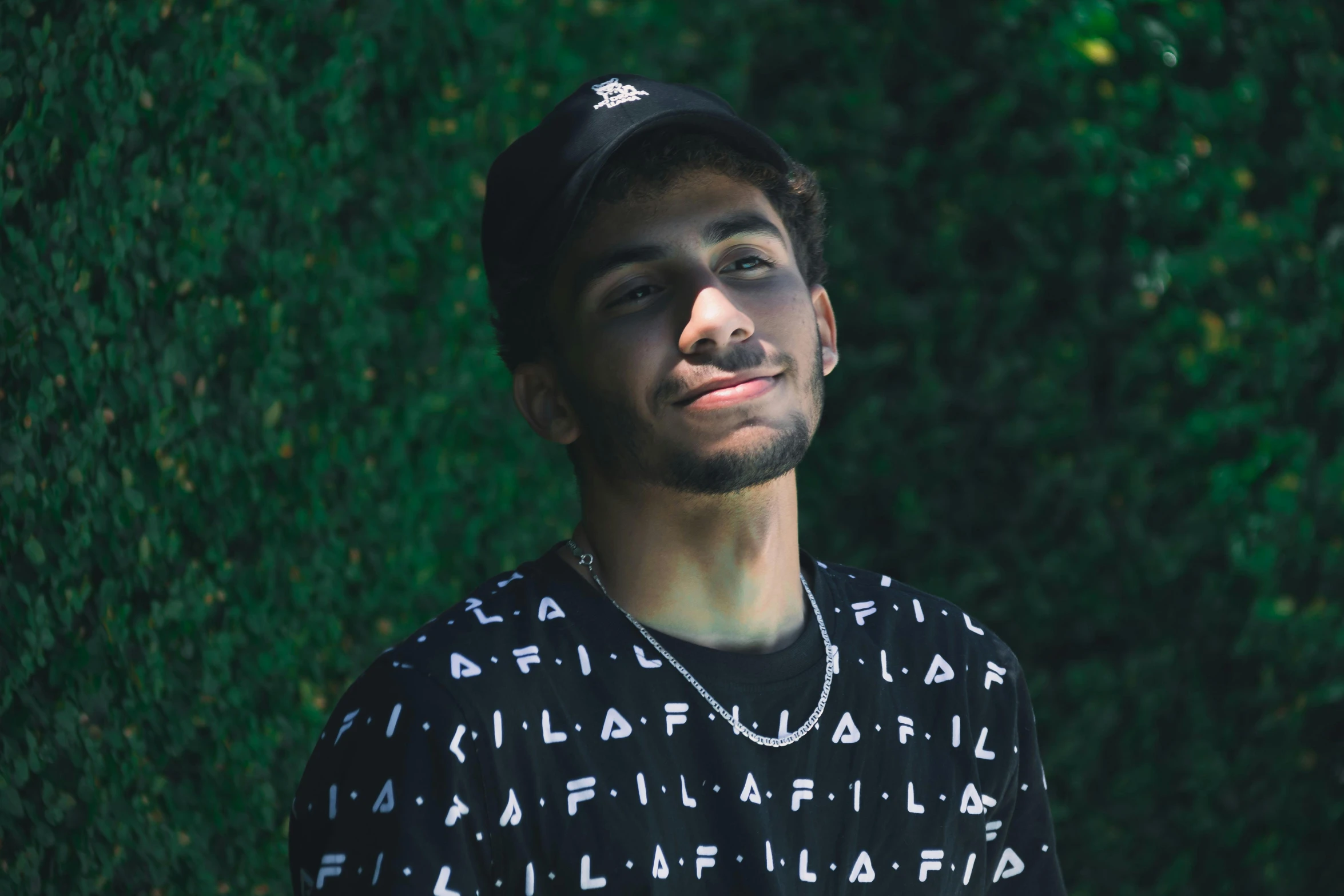 a young man standing in front of greenery