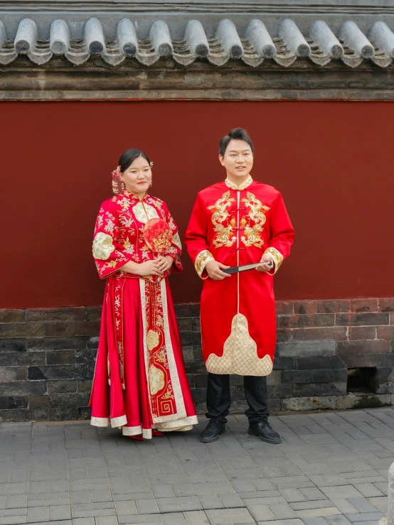 two asian couples wearing traditional clothing in front of a red building