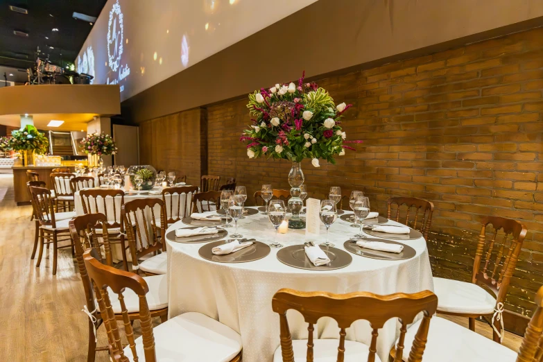 a dining table covered in white linens with lots of place settings and flowers on top