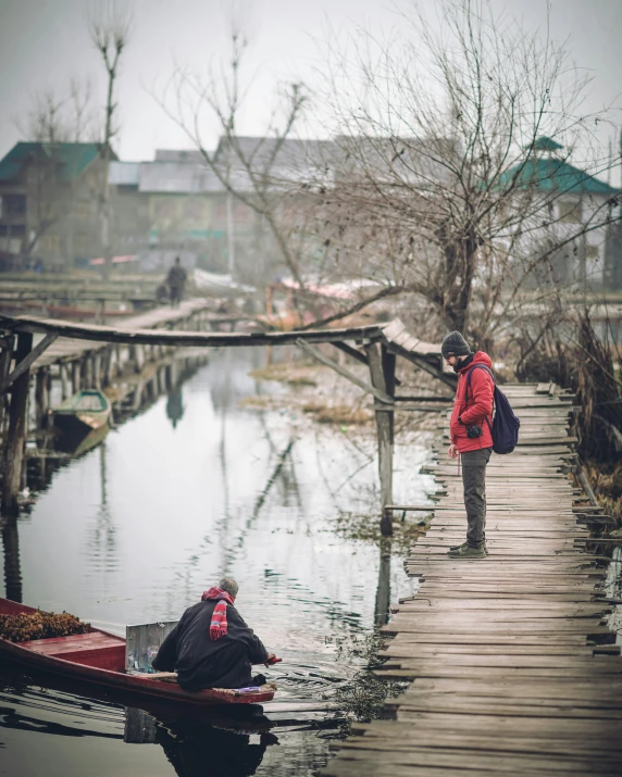 woman walking down bridge in red coat and boots near a body of water