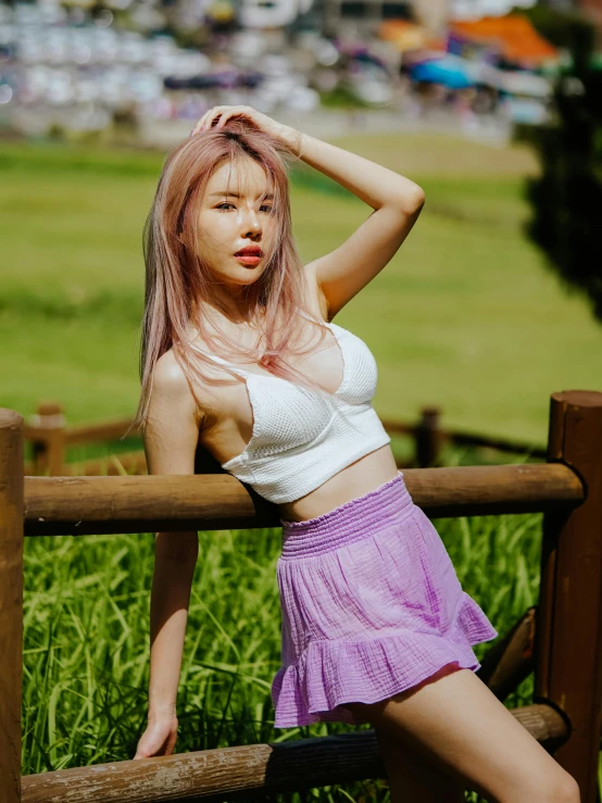 a young woman with pink hair and wearing a white shirt posing against a fence