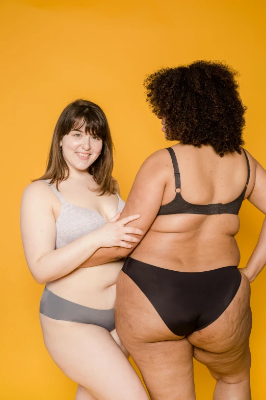 two women in panties stand against a yellow background