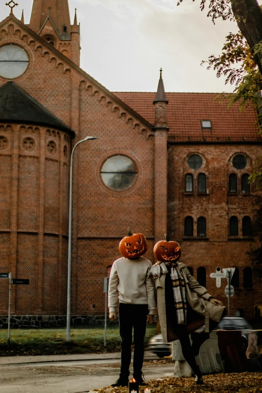 two women with pumpkin heads on are looking at a building