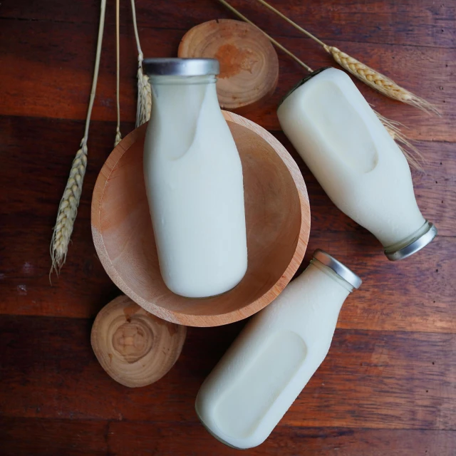 three milk bottles and some wheat on top of a wooden table