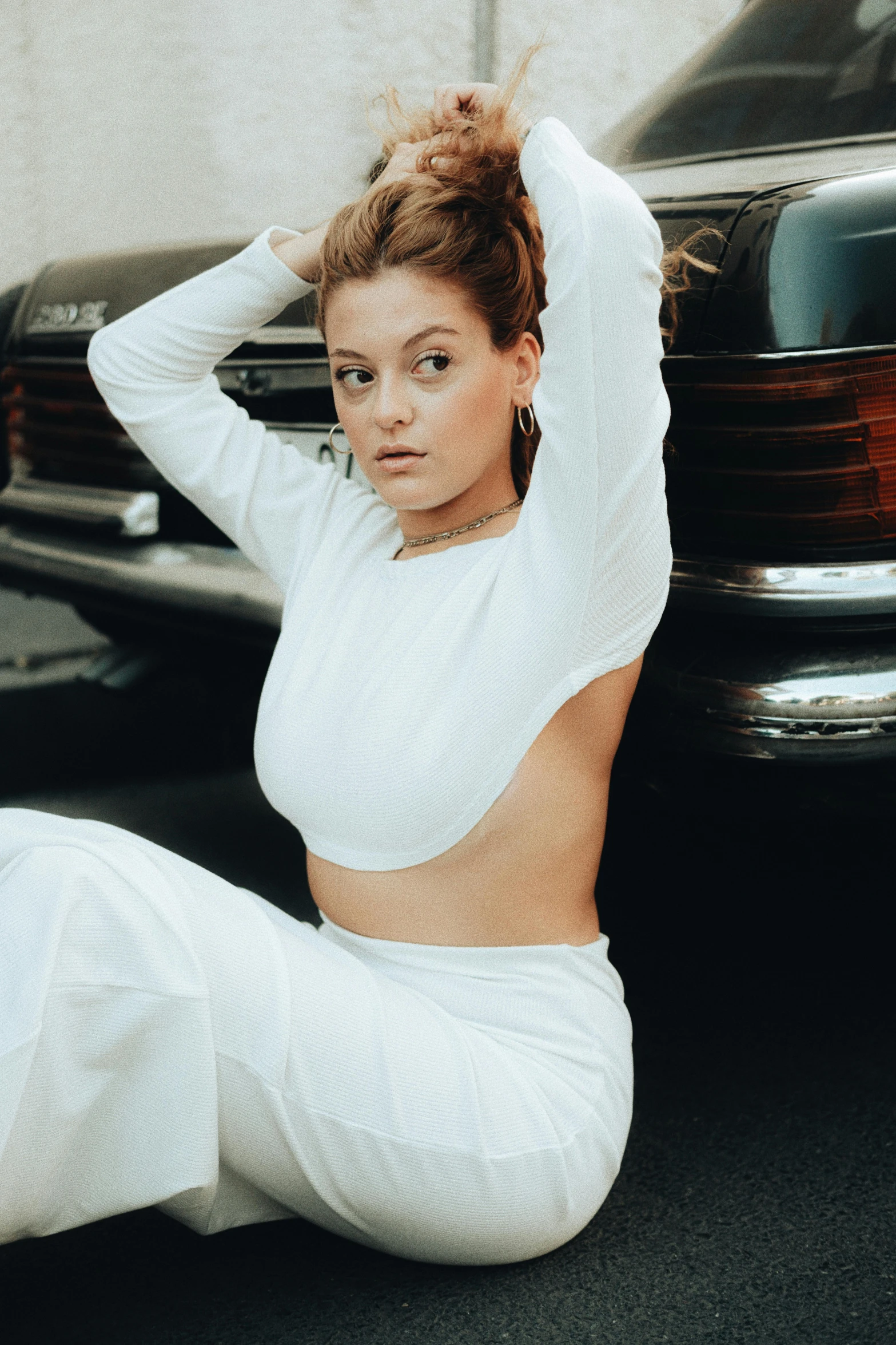 a woman in white poses in front of a car