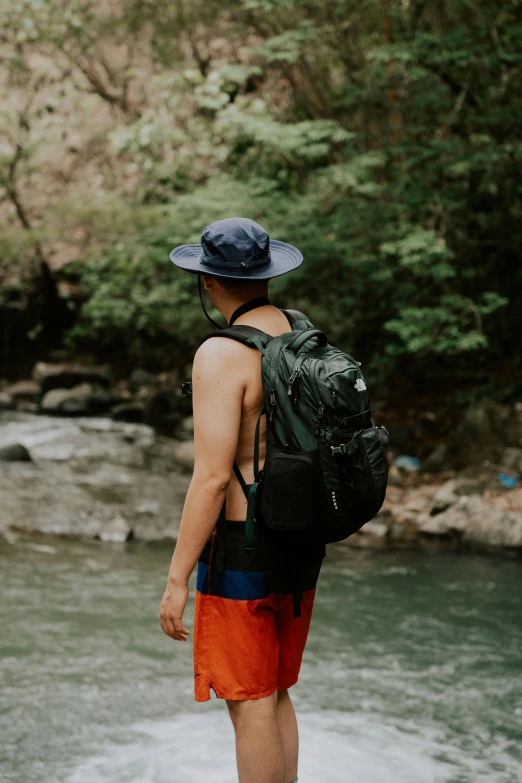 man wearing backpack and standing by stream