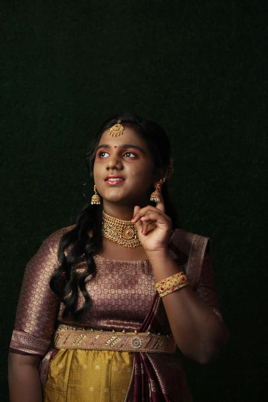 a woman wearing a yellow outfit is dressed in gold jewelry and holds her hands near her eye