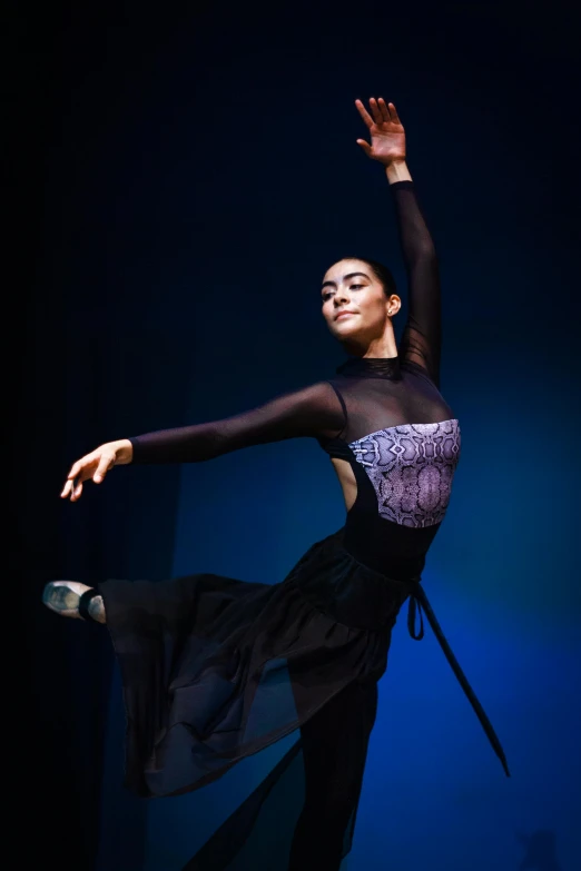 a woman in black dancing on stage with her arm extended