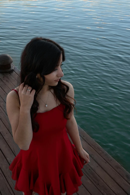 the girl in the red dress is standing by the water