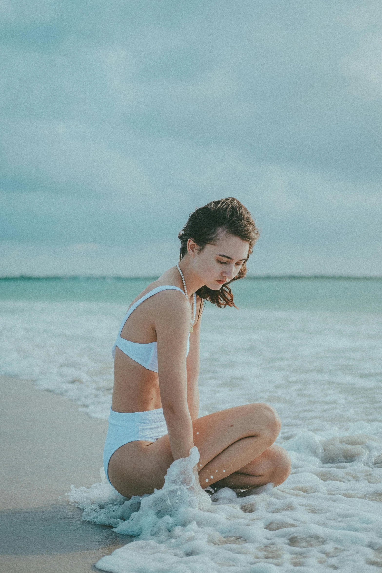 a beautiful young woman sitting in the water on a beach