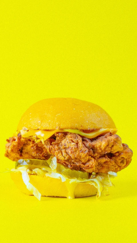 a fried chicken sandwich with pickles on a yellow background