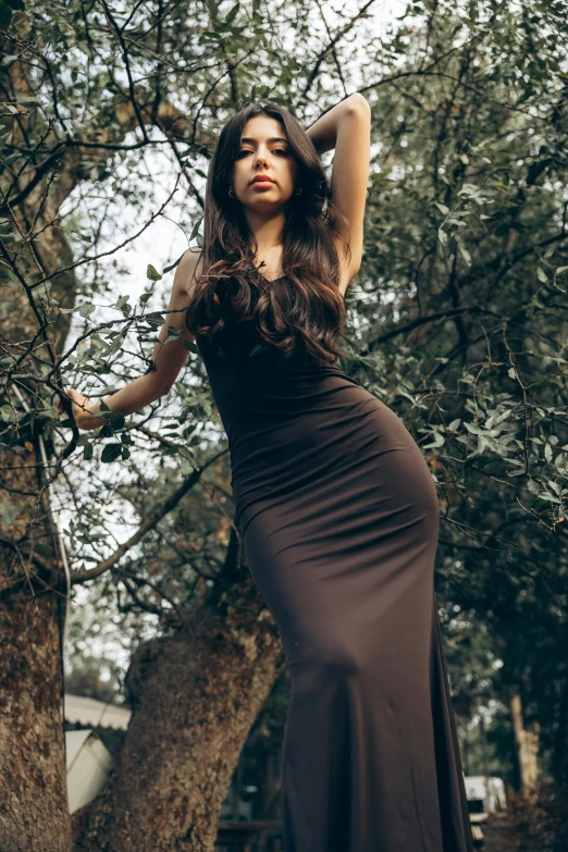 a beautiful woman in a long dress standing by some trees