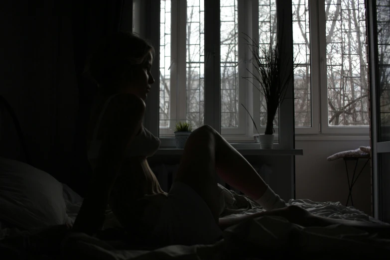 a woman sitting in bed, in front of a window