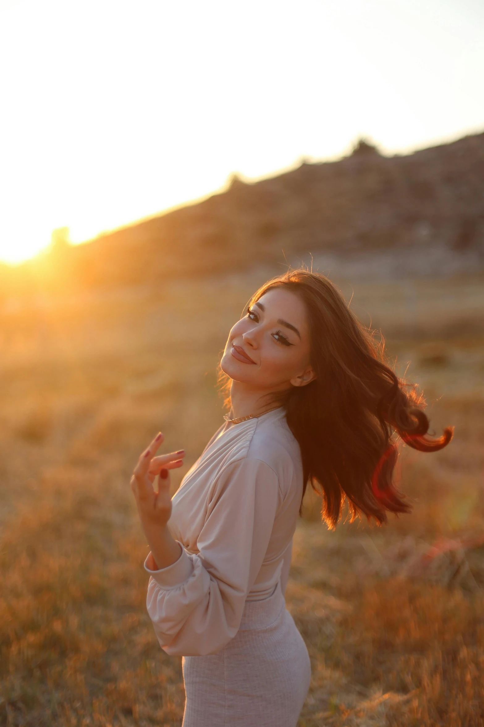 a woman in a field at sunset waves and smiles