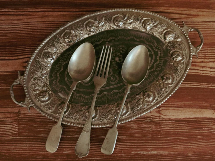 a silver plate with three spoons and a couple of forks