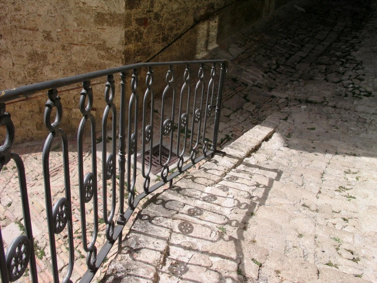 a wrought iron railing on the sidewalk with a stone path