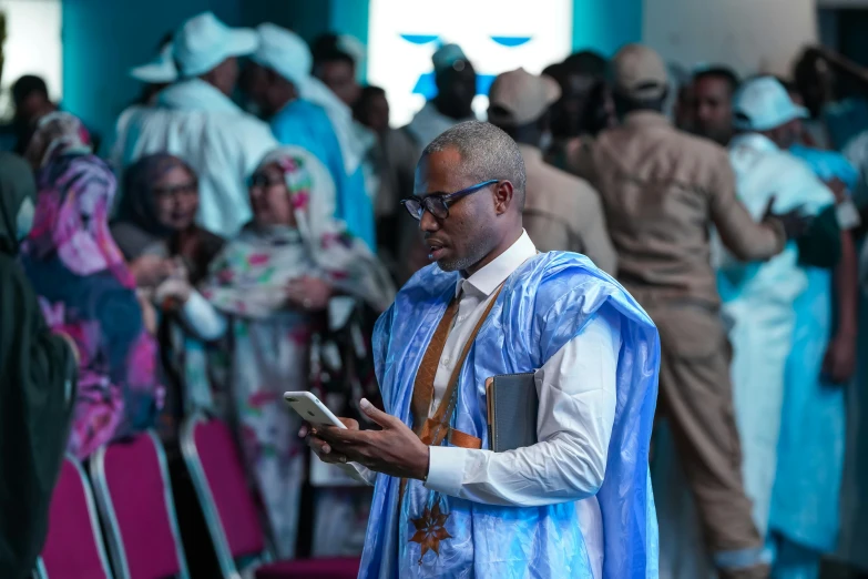 an older man dressed in blue wearing a crown using his phone