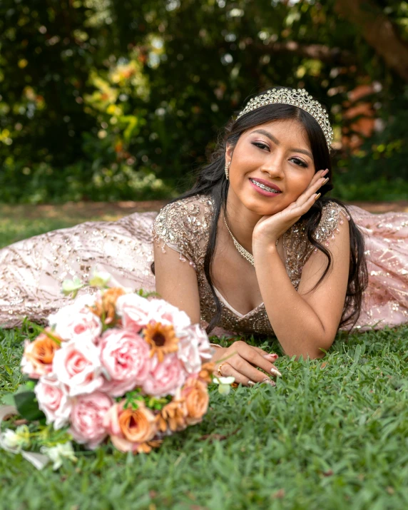 an asian bride in an intricate pink and gold gown lies on grass and looks forward