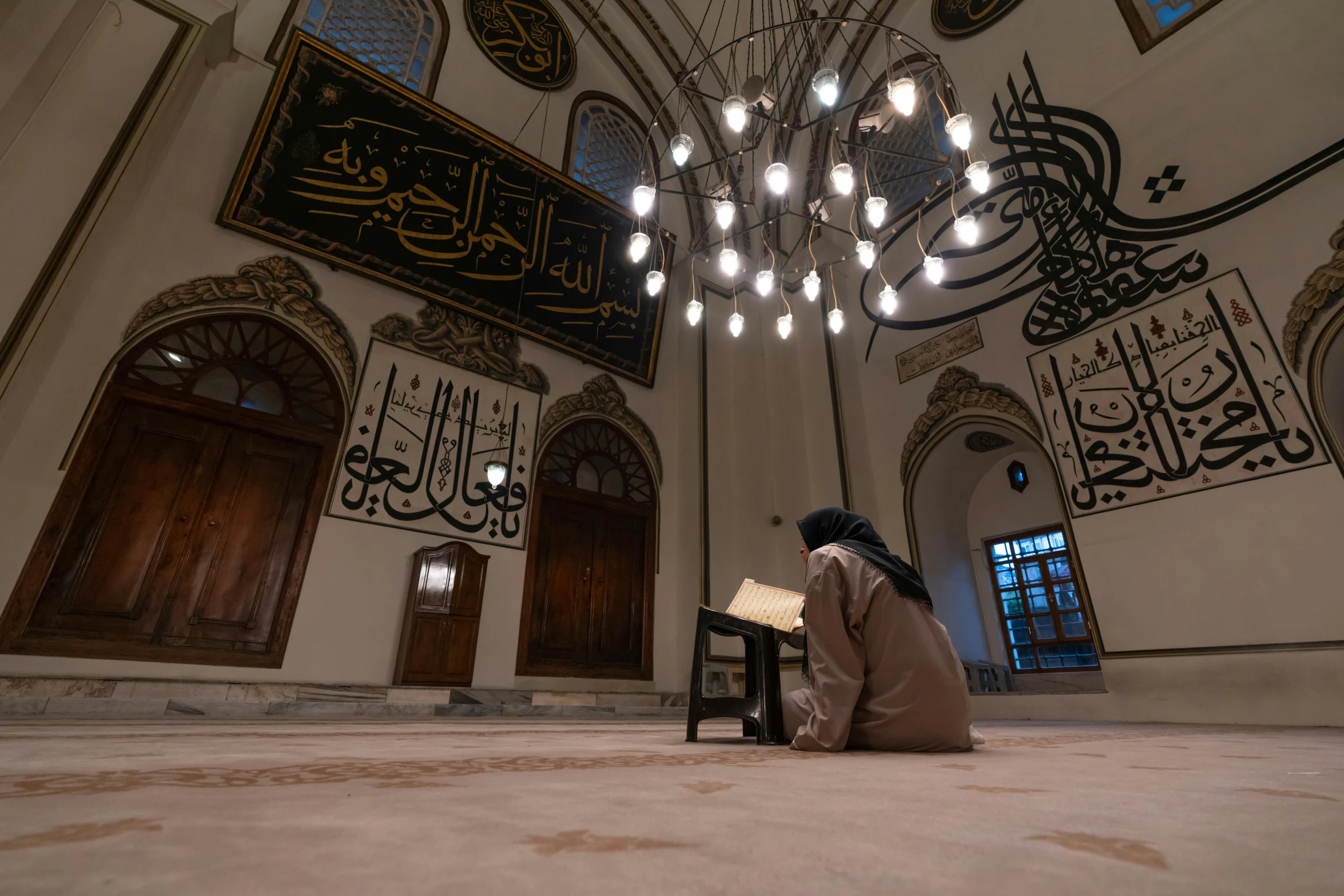 a man sitting on the floor under a chandelier in a mosque