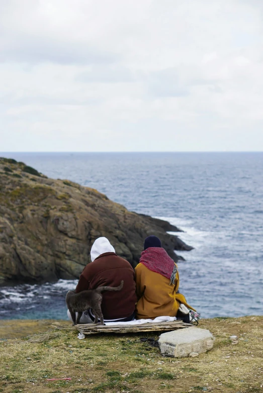 two people sitting on the grass by the ocean