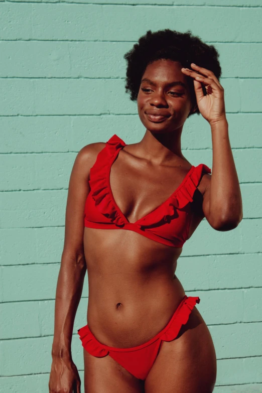 a black woman in a red bikini stands by a blue building