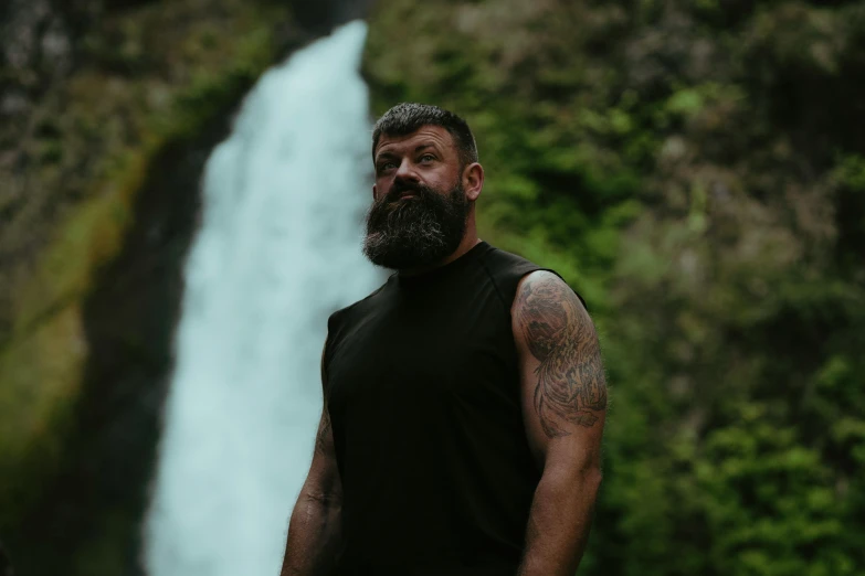 the bearded man stands in front of a waterfall