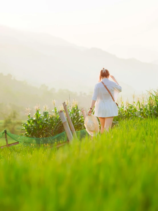 a woman walking through tall green grass towards some mountains