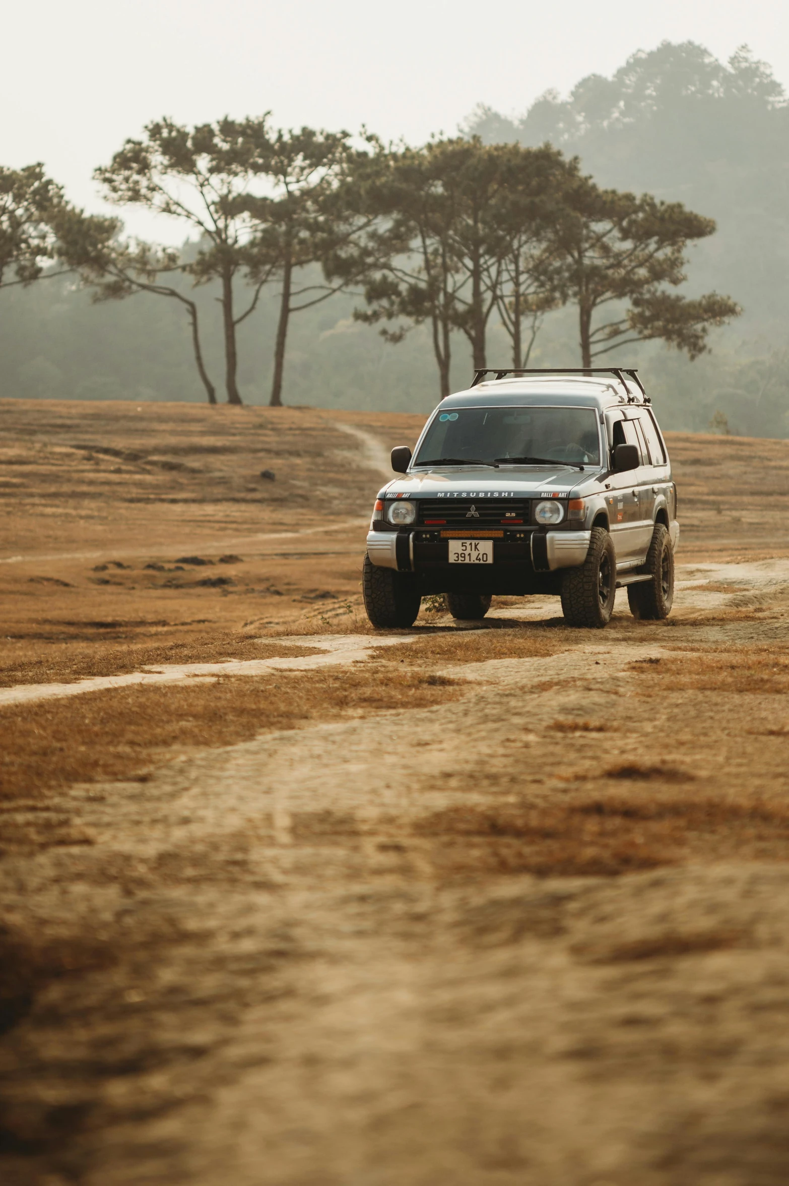 a truck drives on the dirt road through trees