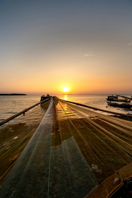 the sun setting behind a wooden dock on a body of water