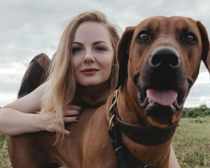 the woman is posing with her dog on a cloudy day