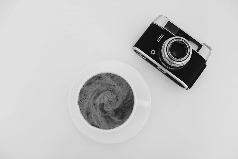 black and white pograph of camera next to coffee