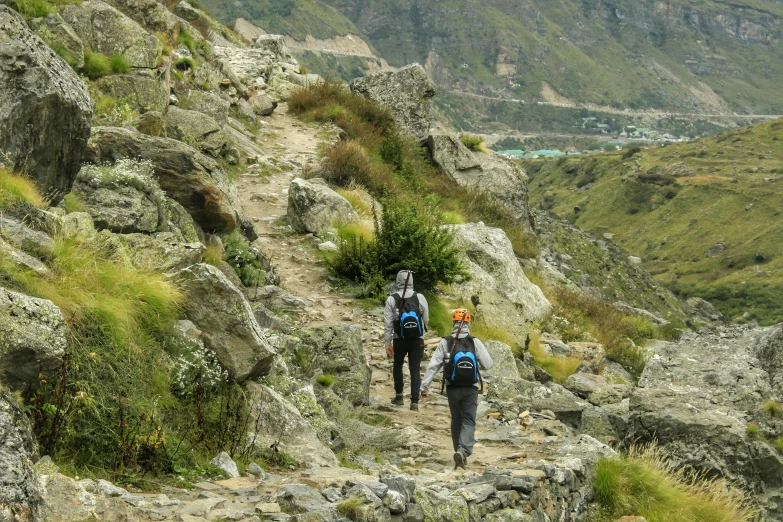 two men with backpacks are hiking up a rocky slope