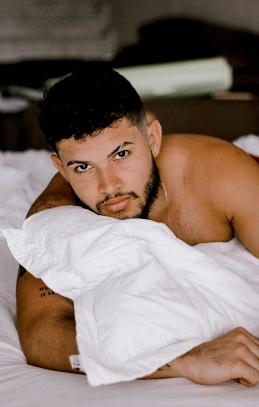 a shirtless man with a white shirt on, lying in a bed