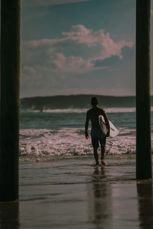 the man walks through the water with his surfboard